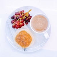 a plate with a muffin, grapes and a cup of coffee