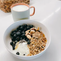 a bowl of granola, blueberries and a cup of milk
