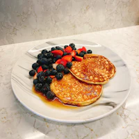 pancakes with berries and syrup on a white plate