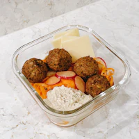 a glass bowl with meatballs, radishes, and cheese