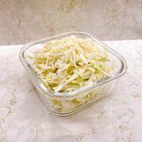 shredded cabbage in a glass bowl on a marble countertop