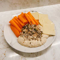 hummus with carrots and cheese on a white plate
