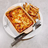 a white plate with a dish of lasagna and french fries