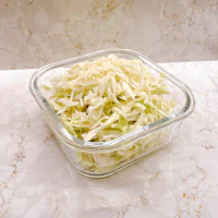 shredded cabbage in a glass bowl on a marble countertop