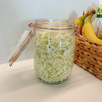 a jar of cabbage in a basket next to bananas